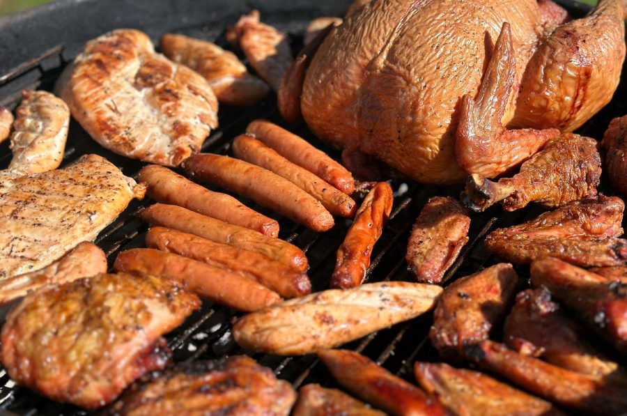 A whole chicken, breasts, thighs, drumsticks, wings and sausages cooking together on a round charcoal grill.
